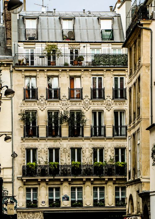 Free Elegant Parisian building facade with ornate details and lush greenery on balconies, captured in daylight. Stock Photo