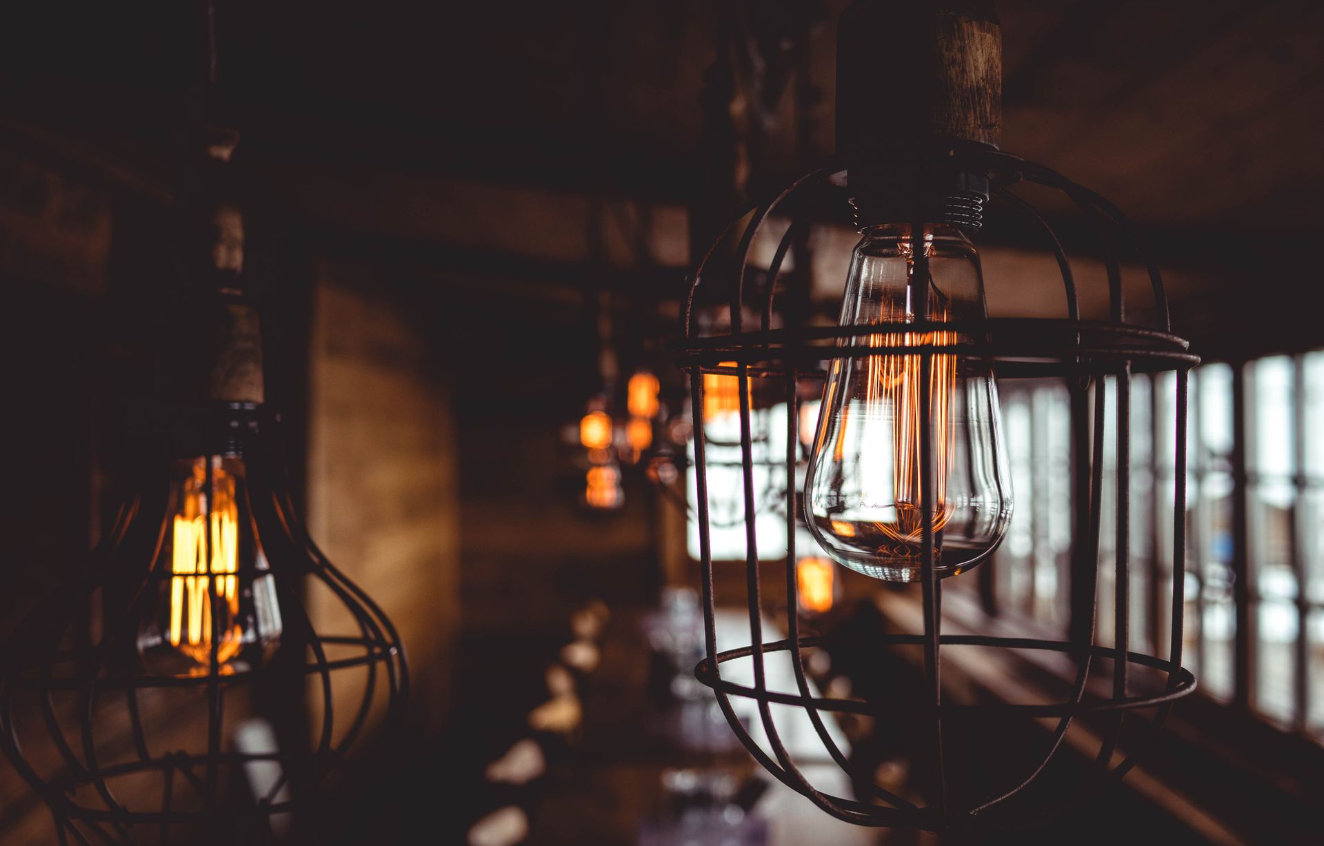 Cozy vintage-style indoor lighting with metal cage pendant lamps, softly glowing filament bulbs.