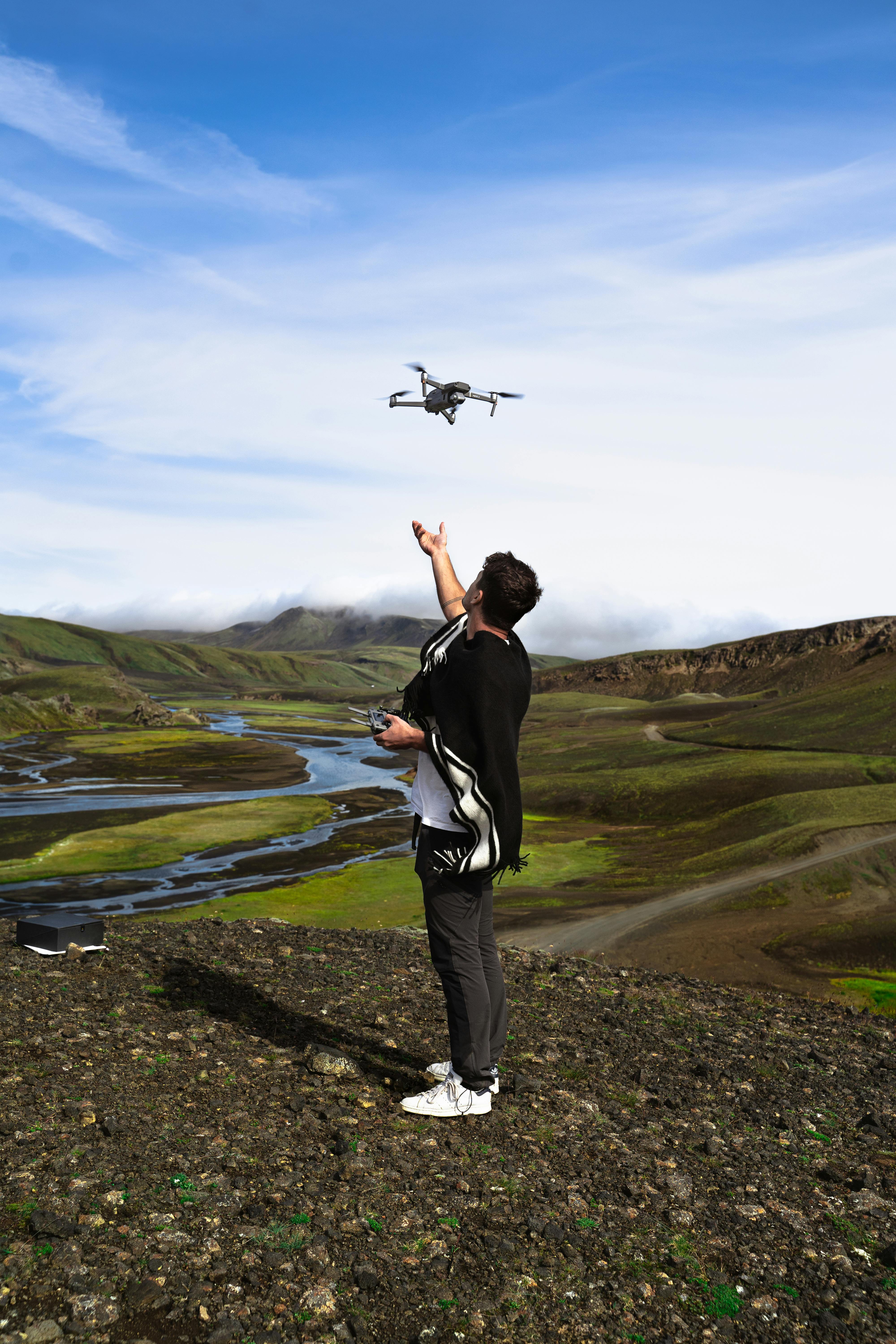 man in black jacket and gray pants standing on green grass field flying drone