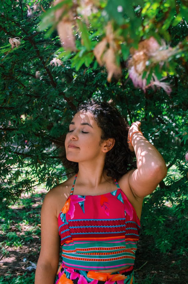 Woman in Red and White Tank Top Standing Under Green Tree