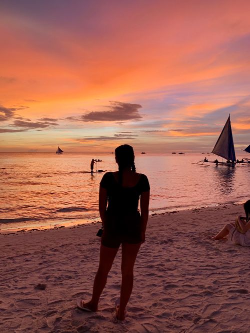 Free Silhouette of anonymous female standing on sandy beach and relaxing against waving sea and cloudy sunset sky on resort Stock Photo