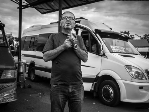 Free Black and white adult man with money standing near van and smoking while resting on bus station Stock Photo