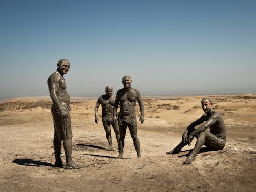 Men Covered in Mud Standing on Brown Sand