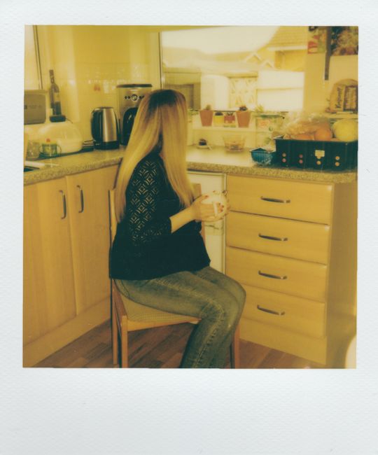 A young woman with long blonde hair enjoys a warm drink in her cozy kitchen.