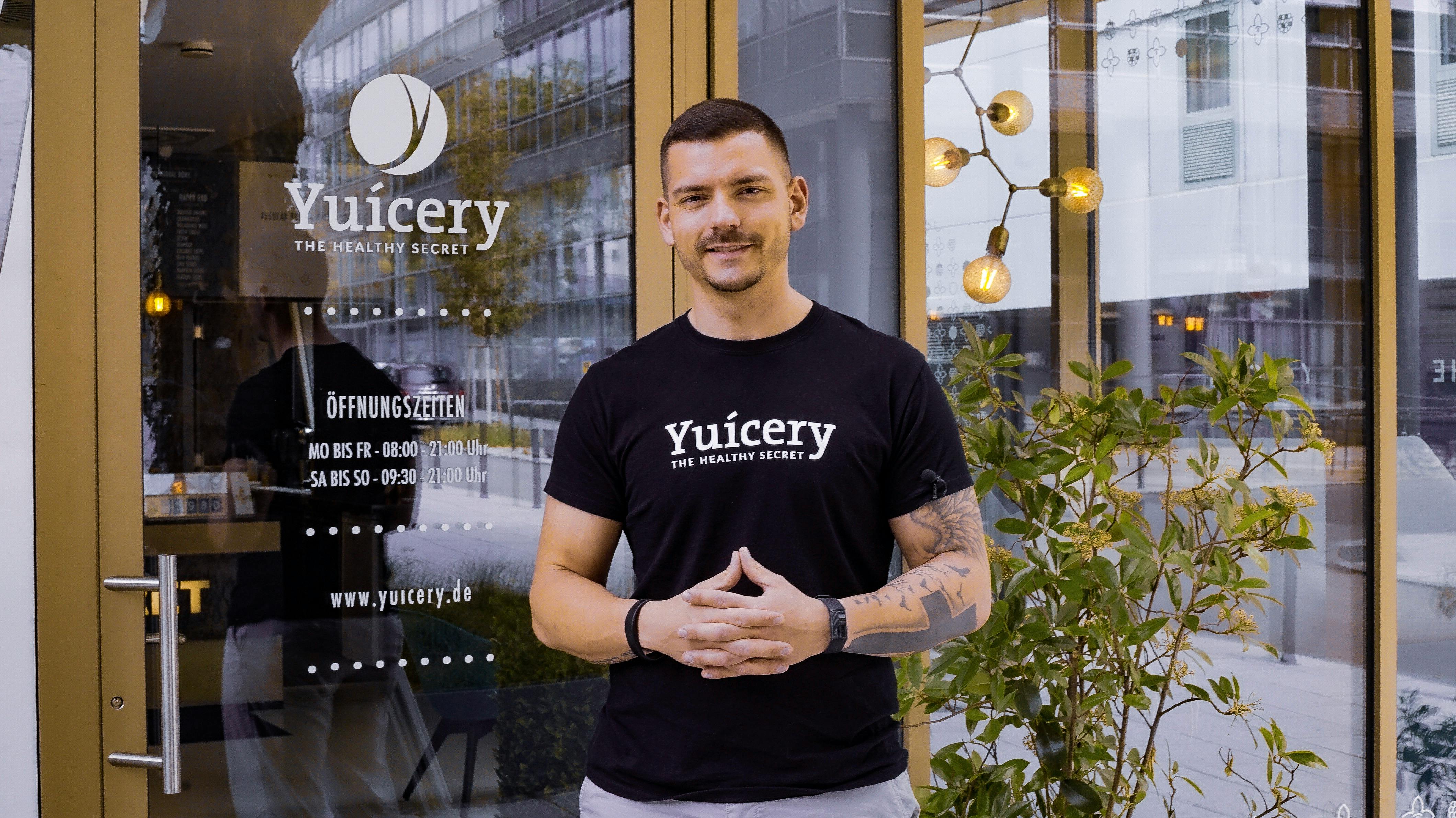 Smiling man stands by the Yuicery cafe entrance, promoting healthy lifestyle in a modern setting.