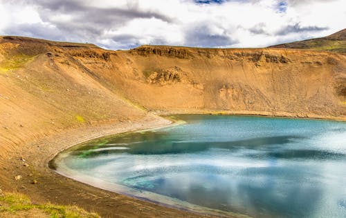 Brown Mountain Near Body of Water Under Cloudy Sky