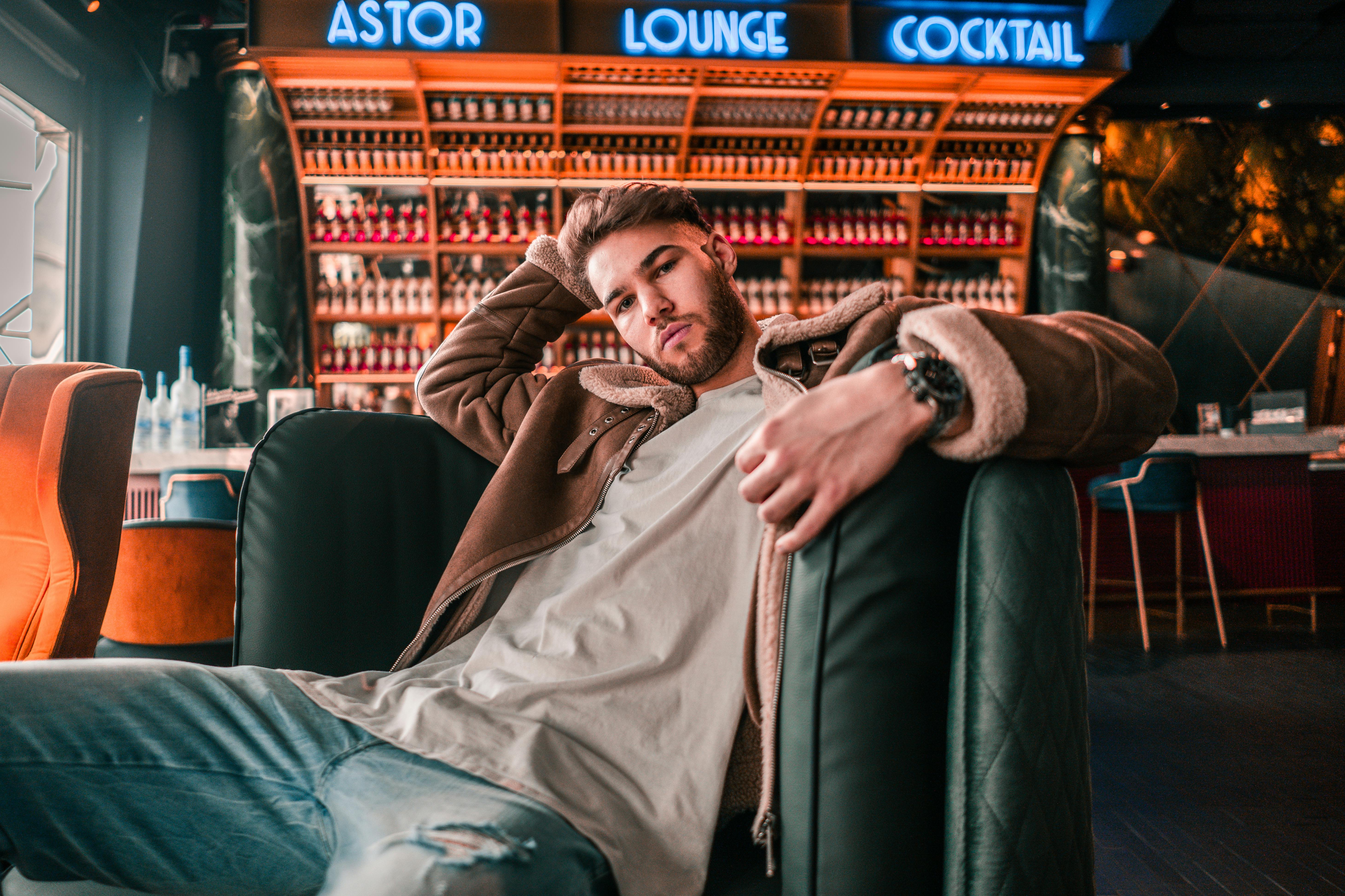 man in brown coat lying on black leather couch