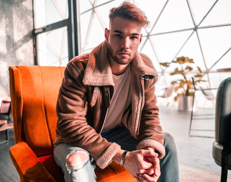 Man In Brown Coat Sitting On Orange Chair