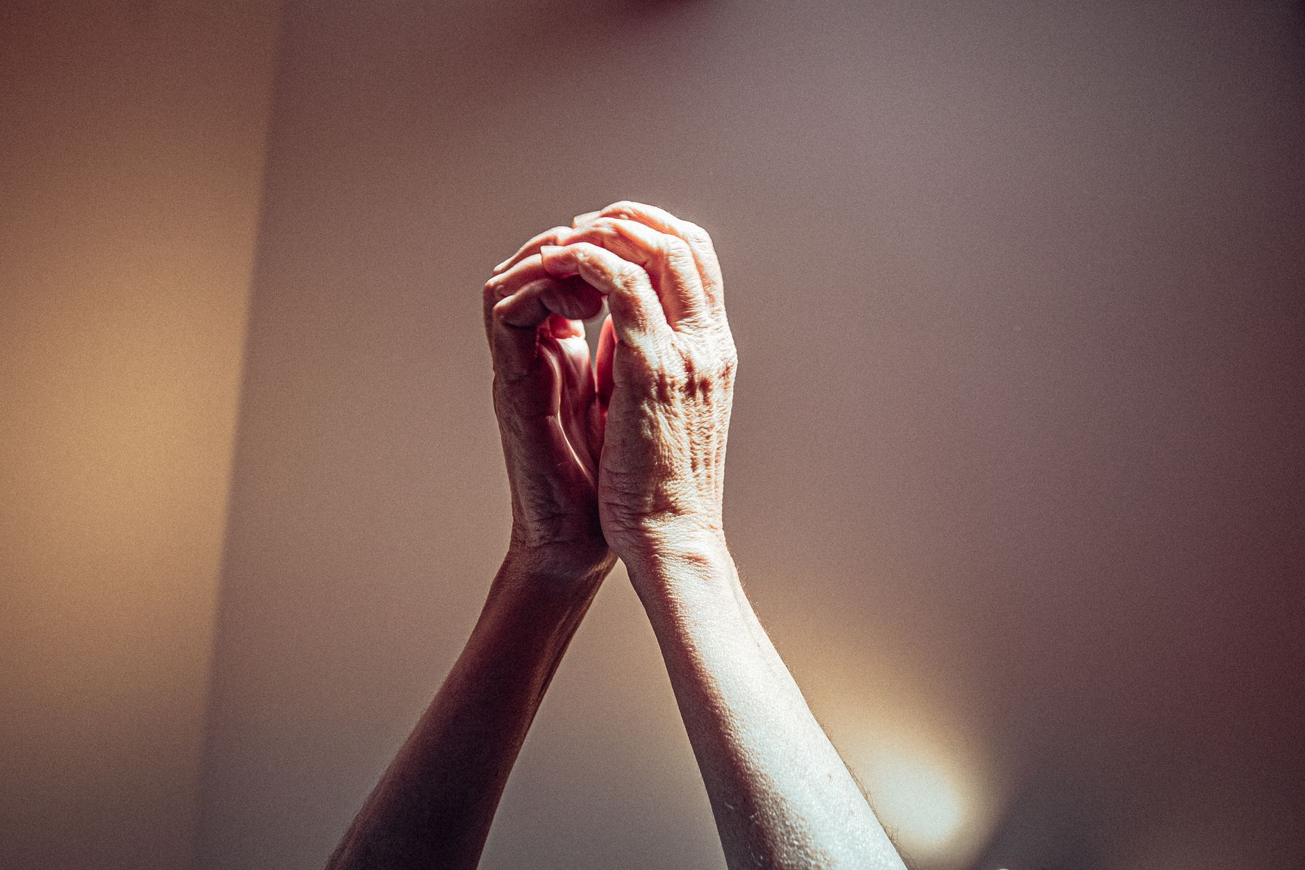 nad longevity protocol — Close-up of elderly hands clasped in prayer with dramatic lighting highlighting wrinkles.