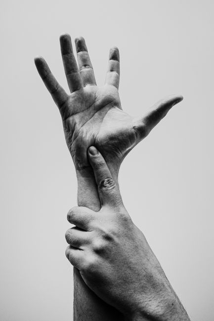 Black and white close-up of hands in a conceptual pose, emphasizing gesture and texture.