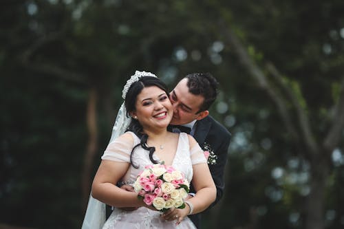 Free Man in Black Suit Hugging Woman in White Floral Wedding Dress Stock Photo