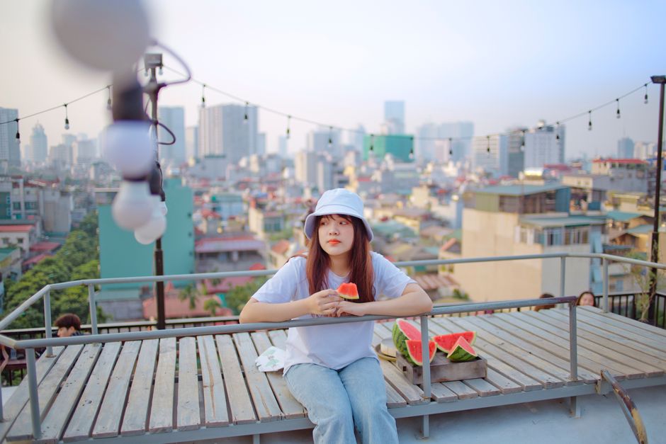 Woman enjoying watermelon on a rooftop with cityscape view, embracing summer vibes.