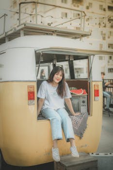 Casual scene of a young woman sitting on a vintage van with watermelon, enjoying a sunny urban day.