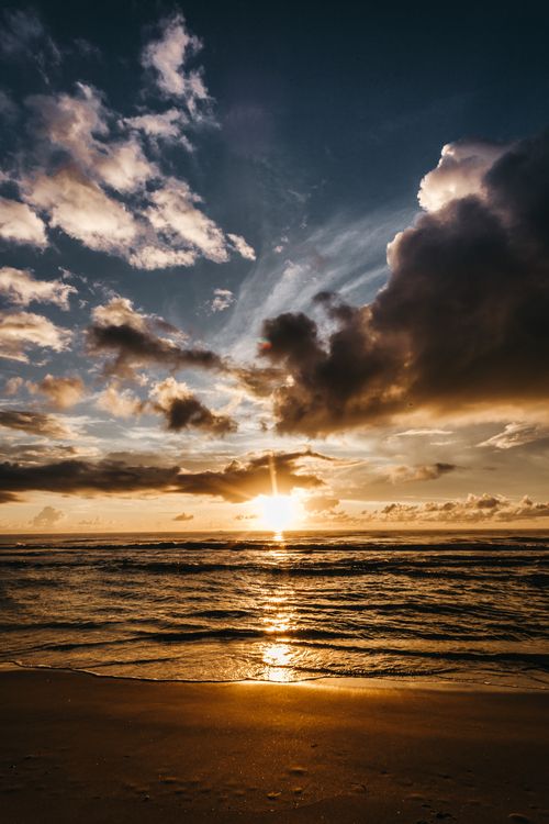 Free Bright evening sun shining on cloudy sky over waving sea and sandy beach in nature Stock Photo