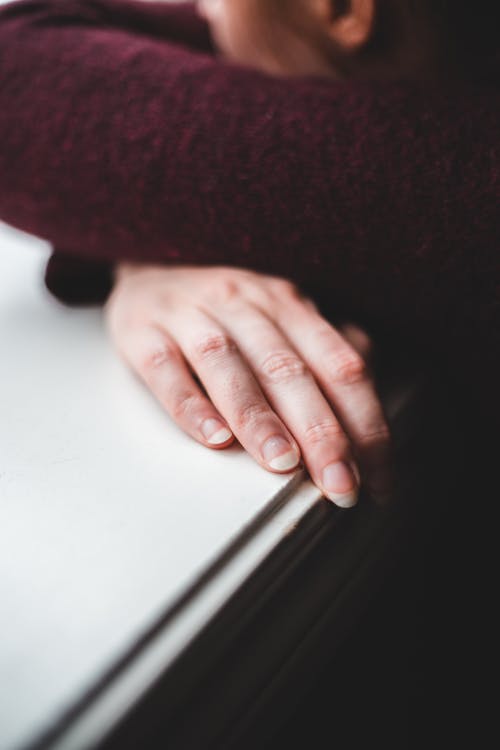 High angle of anonymous person with long nails leaning on windowsill and relaxing on calm day at home