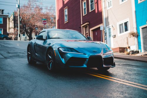 Free A blue Toyota Supra parked on a wet city street, showcasing its elegant design against colorful houses. Stock Photo