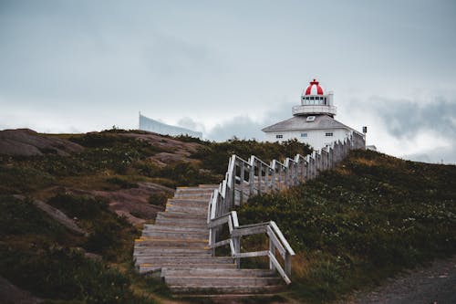 Shabby lumber stairs going on hill to house with beacon against cloudy evening sky