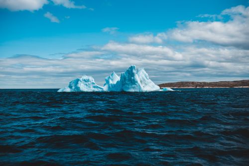 Free A stunning iceberg floating in a deep blue ocean under a partly cloudy sky, capturing nature's beauty. Stock Photo