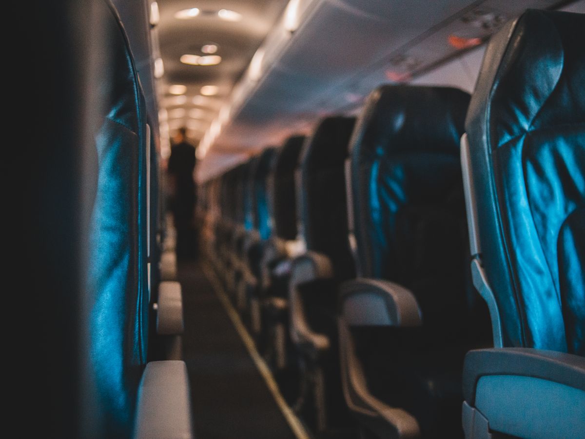 Empty aircraft cabin aisle with rows of blue seats and a passenger walking towards the rear