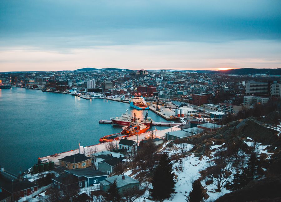 Modern city with port located on seashore covered with snow against sunset sky in winter evening