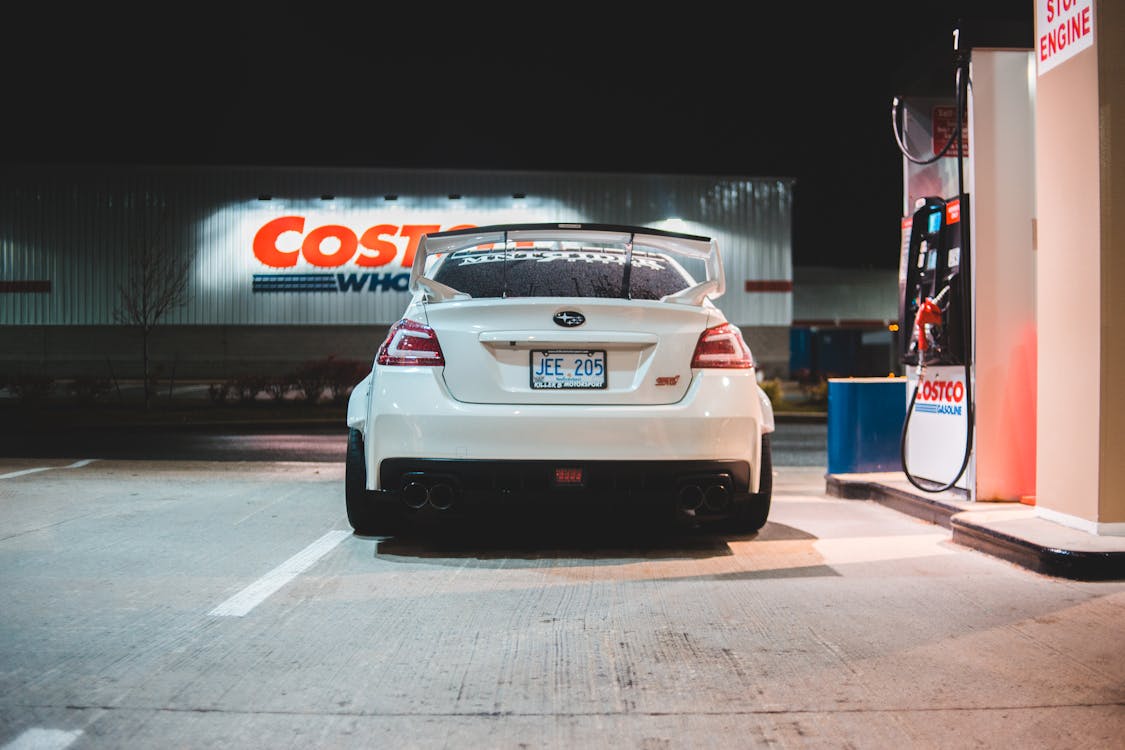 Free Contemporary white car parked near pump on fuel station at night in city Stock Photo