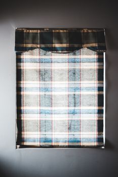 Minimal interior of white wall with square window shut with checkered simple curtain