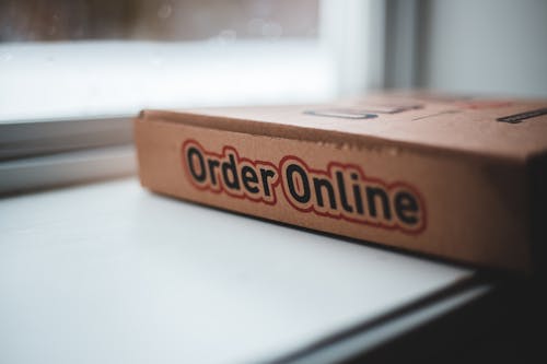 Soft focus of cardboard box of delivery pizza online service placed on white windowsill in daylight