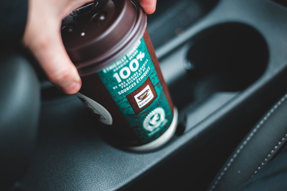Person holding a disposable coffee cup inside a car, showcasing ethical sourced coffee.