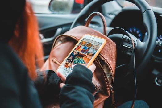 Faceless female driver with backpack sitting at steering wheel and browsing mobile phone