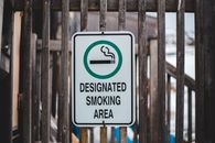 Sign with cigarette in green circle allowing to smoke in designated area hanging on wooden fence