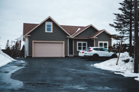 Exterior of small residential house in neighbourhood with cars parking on snowy ground in misty day