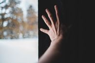Tender hand on background of black wall reaching out near window with view of woods in winter