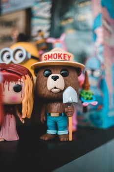 Cute toy bear with shovel on shelf with collection of movies and cartoon heroes