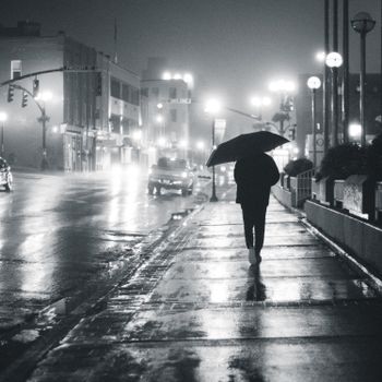 夜晚，打着伞走在潮湿人行道上的剪影，与路灯和车灯一同亮着