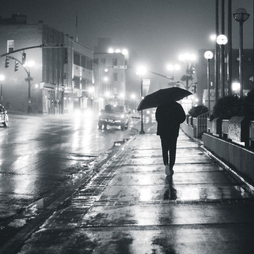 Figure with an umbrella under glowing street lamps at night