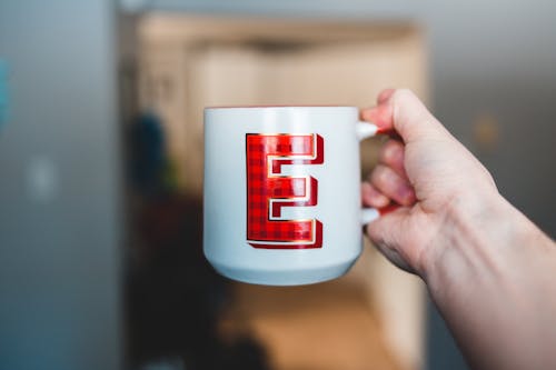 Free Hand of person holding white ceramic cup with tartan letter E at home Stock Photo
