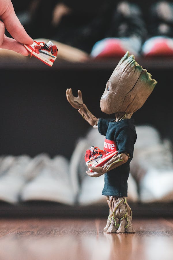 Crop fan giving small sneakers to small plastic comic tree character dressed in t shirt