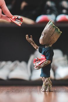 Crop fan giving small sneakers to small plastic comic tree character dressed in t shirt