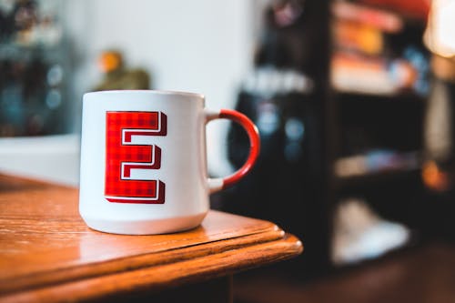 Memorable white mug with red letter E placed on edge of wooden table at home