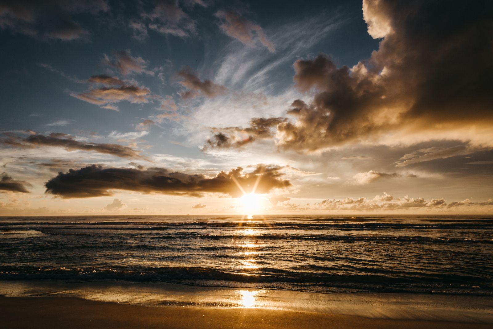 Golden sunbeams above rough waving sea at sunset time with clouds high in sky
