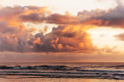 Amazing scenery of waving sea water under glowing fluffy clouds in pink and golden light of sunset