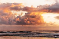 粉红色和金色的日落光线下，闪闪发光的蓬松云层下波光粼粼的海水景色