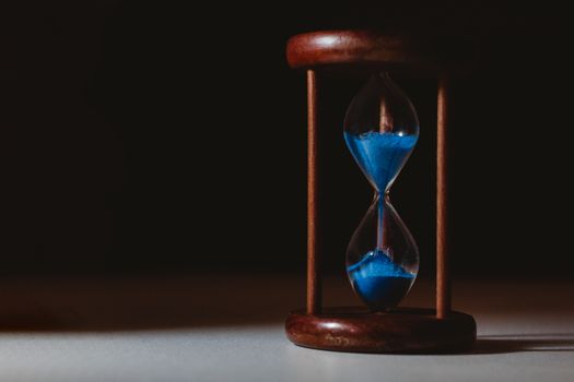 A minimalist close-up of a wooden hourglass with blue sand flowing, symbolizing the passage of time.