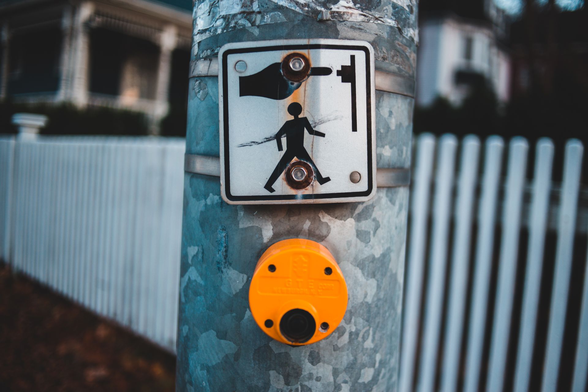 Metal signboard with pedestrian and button on metal pole placed on pavement of crosswalk