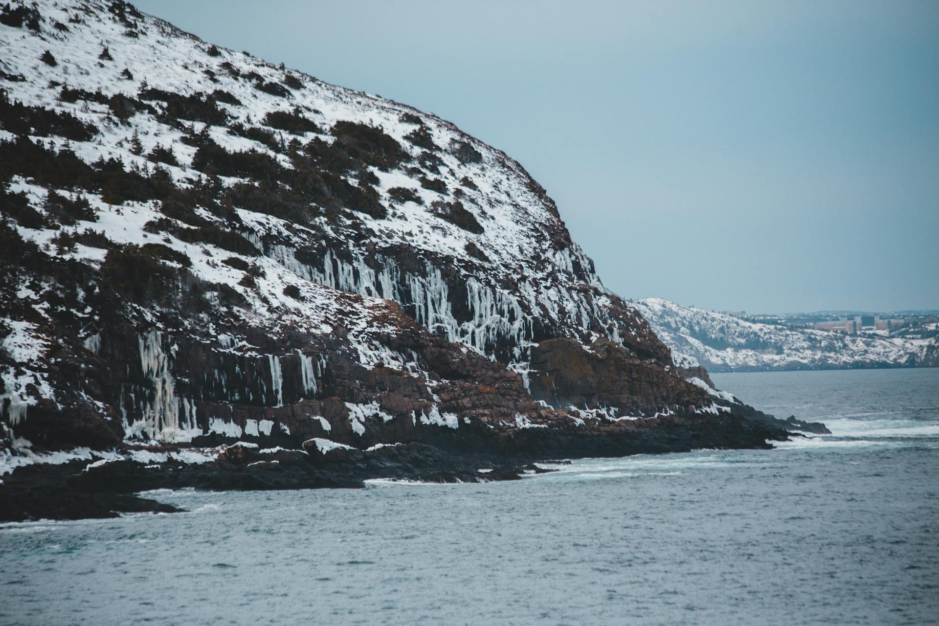 Snow-covered cliffs along the coast with ocean waves, capturing a serene winter seascape.