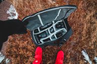 Overhead view of crop anonymous person in bright sneakers opening bag with photo camera and assorted lens on dry grass partially covered with frost in cold weather