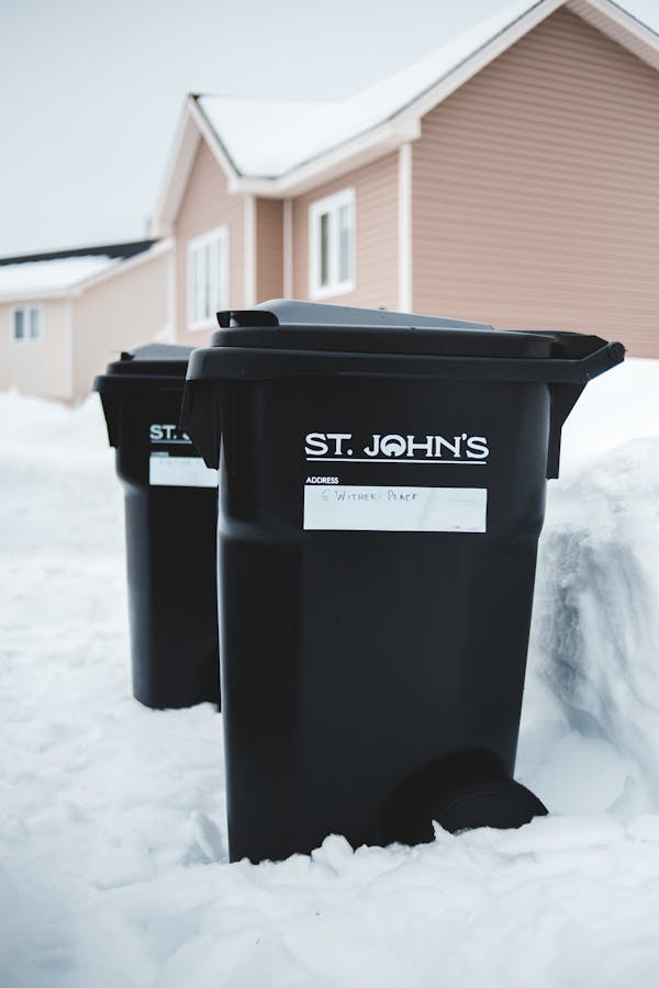 Similar rubbish bins on snow near house facade in town