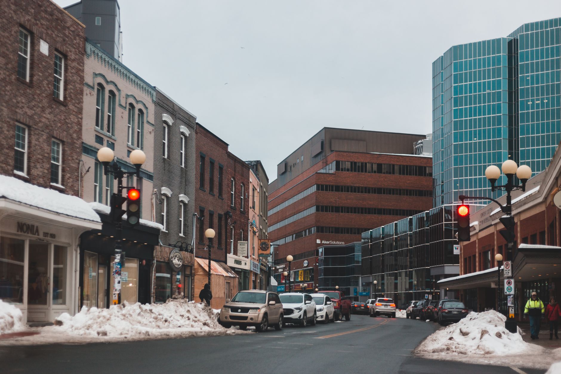 Busy winter street scene in an urban downtown area with snow-covered sidewalks and red traffic lights.