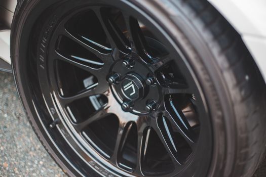 From above of modern automobile black wheel with rubber tire and metal rim with similar shiny spokes on asphalt pavement