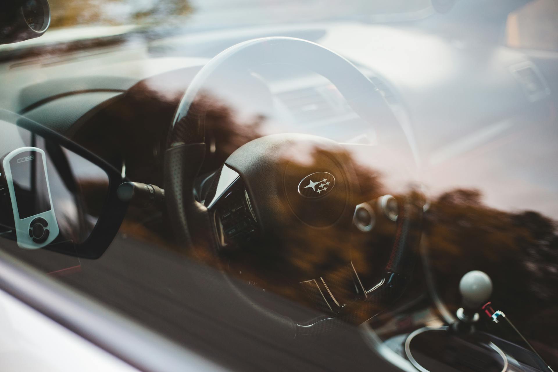 From above through glass view of contemporary auto interior with plastic steering wheel and shiny transmission with window reflecting trees in daylight